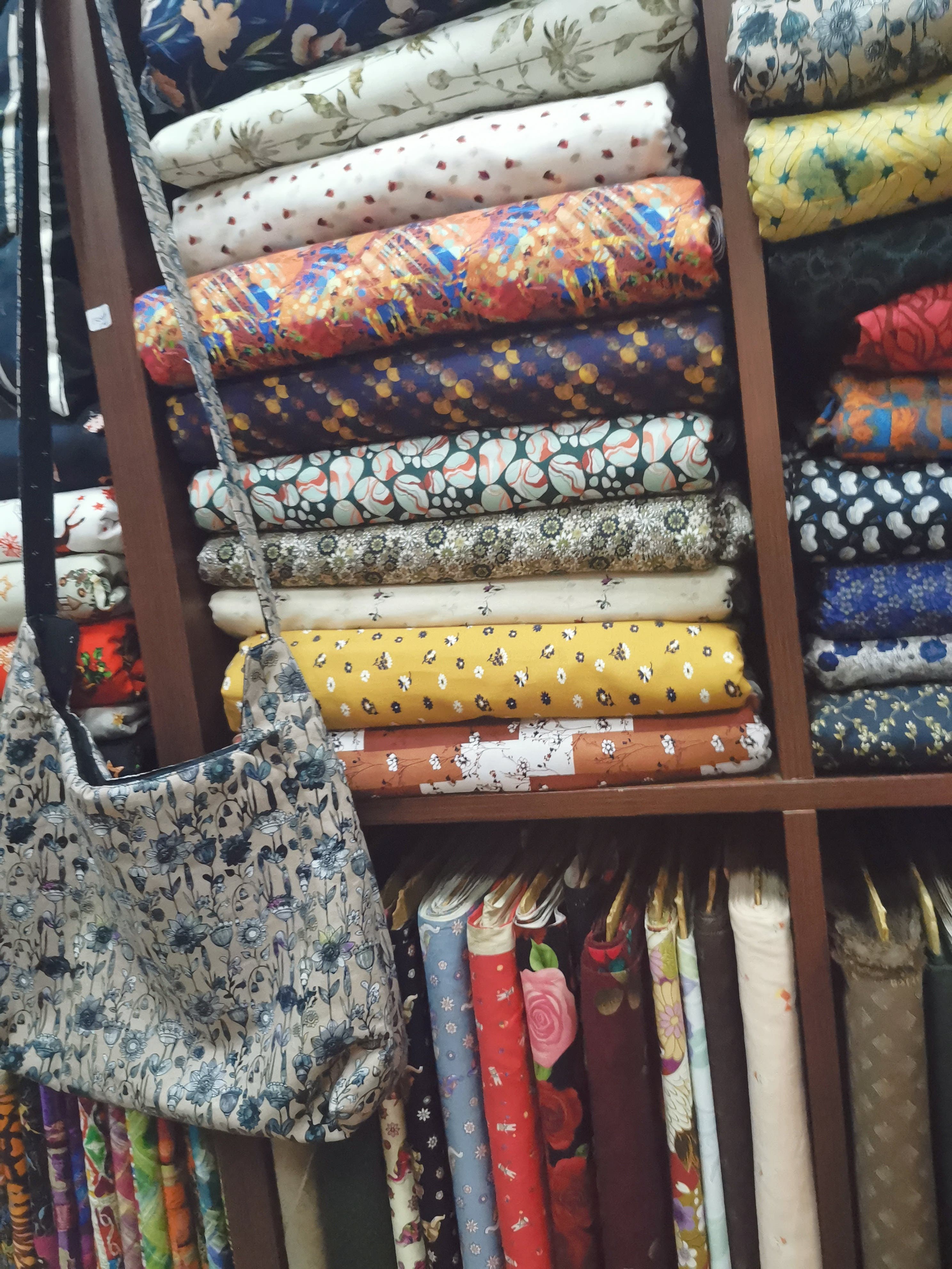 Rolls of printed cotton stacked in wooden pigeonhole shelving at a fabric shop, with bolts hanging below